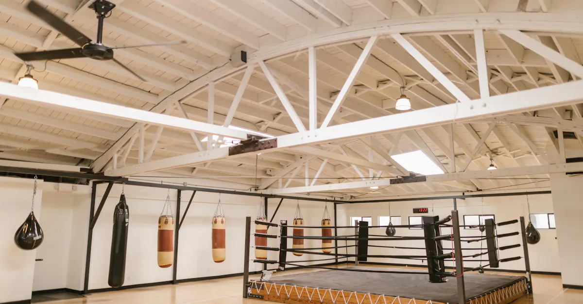A clean and empty boxing gym with punching bags and a ring, ready for training.